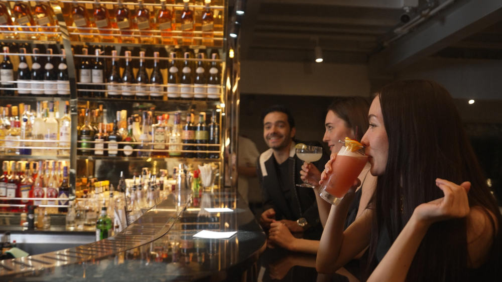 Three friends having cocktails and socializing at a well-stocked Texas bar in a restaurant.