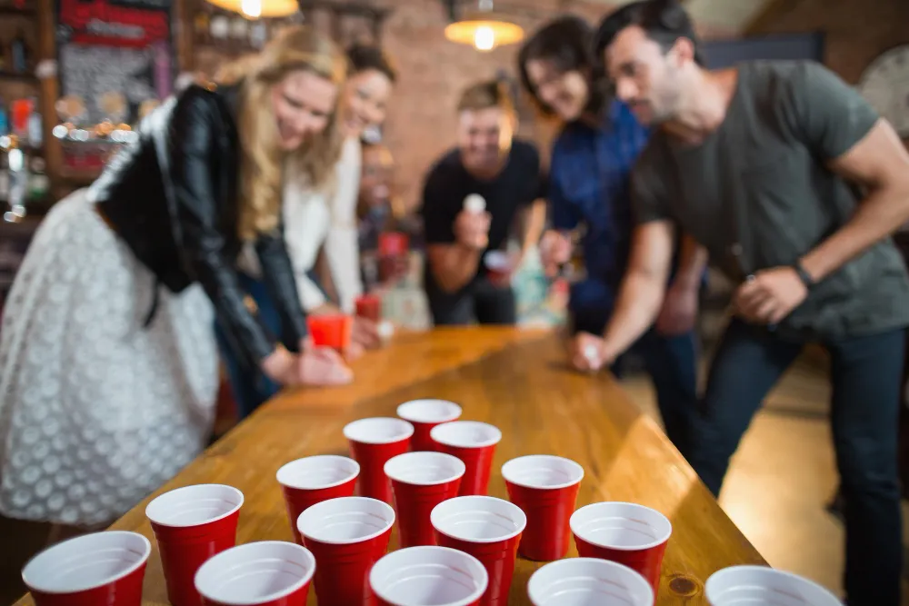 A large group of friends engaged in a game of beer pong, an example of effective bar entertainment ideas that boost customer engagement.